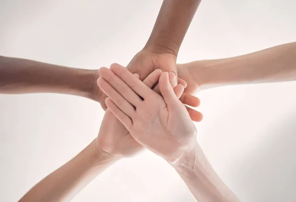 Group of diverse businesspeople piling their hands together in an office at work. Business professionals having fun standing with their hands stacked for support and unity from below.