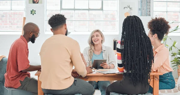 Group of diverse businesspeople having a meeting in a modern office at work. Young happy caucasian businesswoman smiling while working on a digital tablet in a boardroom with colleagues. Creative