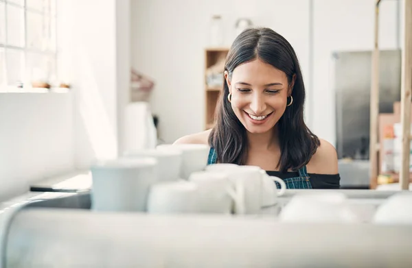 One happy hispanic waitress using a coffee machine to prepare a hot beverage in a cafe. Happy barista making a warm drink to serve customers in a coffeeshop.