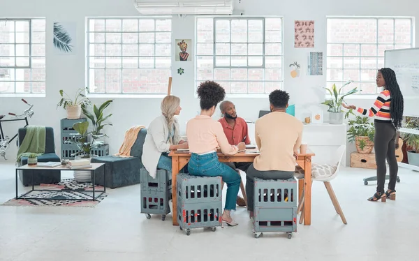 Group of diverse businesspeople having a meeting in a modern office at work. Young african american businesswoman doing a presentation of an idea on a whiteboard in a boardroom with colleagues