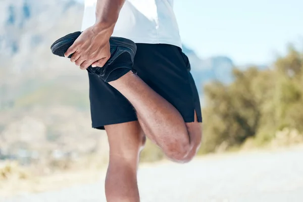 Closeup of an unknown man standing alone and stretching during his outdoor workout. Fit male warming up before a run outside.