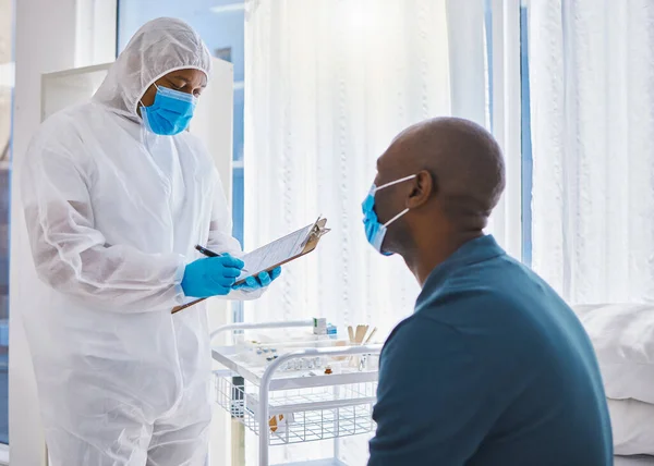 Doctor writing a patients information on their chart. Patient talking to a doctor during a checkup. Patient in checkup for covid symptoms. Patient in medical exam with a gp specialist.