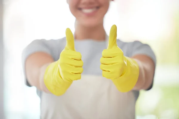 An unrecognizable domestic worker showing the thumbs up while wearing gloves and cleaning. One unknown mixed race woman looking happy while cleaning her apartment.