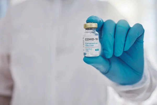 Hand of a doctor holding a vial of covid vaccine. Ready to cure the world of covid. Closeup on hands of a medical specialist holding cure to corona virus. Disease expert holding a vial of vaccine.