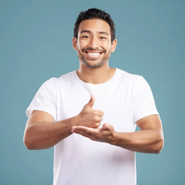 Handsome young mixed race man giving thumbs up while standing in studio isolated against a blue background. Hispanic male showing support or appreciation. Backing or endorsing a product or company.