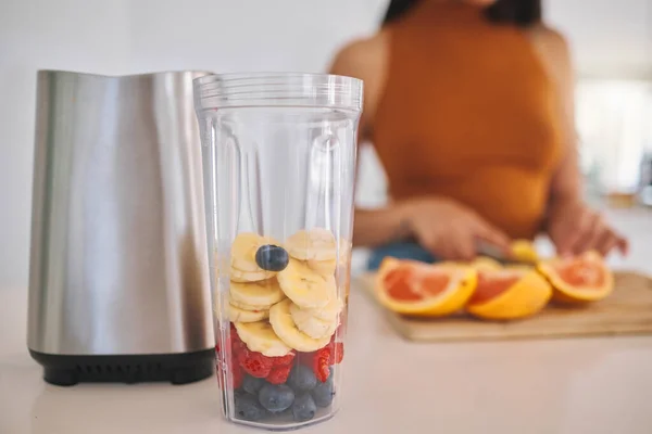 a woman putting a variety of fruits into a blender at home.