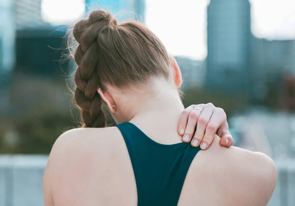 Closeup of one caucasian woman from behind holding neck shoulder while exercising outdoors. Female athlete suffering with painful injury from fractured joint and inflamed muscles during workout