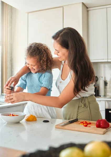 幸せな母親の家庭で台所で調理するために娘を教える お母さんとサラダを作っている間にボウルに調味料コショウグラインダーを追加する女の子 — ストック写真