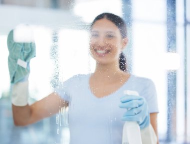 Portrait of a happy mixed race domestic worker using a cloth on a window. One Hispanic woman enjoying doing chores in her apartment. clipart