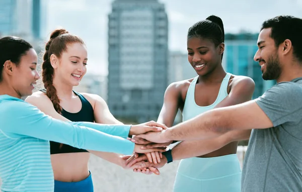 Diverse group of happy sporty people stacking hands together in pile to express unity and support. Motivated athletes huddled in circle for encouraging workout pep talk. Joining for collaboration