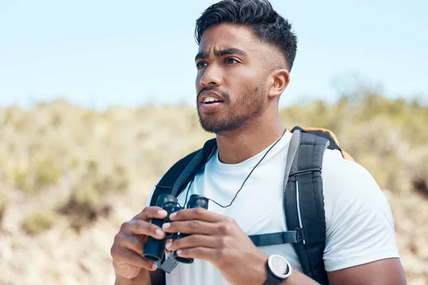 Closeup of a mixed race male using a binocular during a hike outside. Young handsome indian male looking at a view while out on a walk in nature.