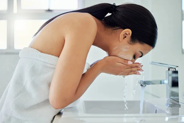 a young woman washing her face in a bathroom at home.