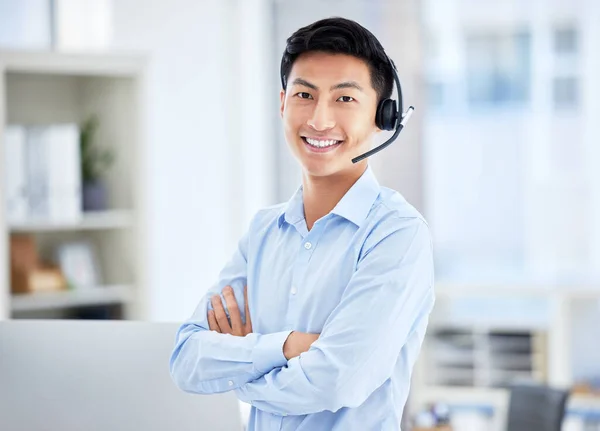 Portrait of asian call centre agent wearing a headset while working in office while stand with arms crossed . Confident and smiling businessman consulting and operating a helpdesk for customer sales