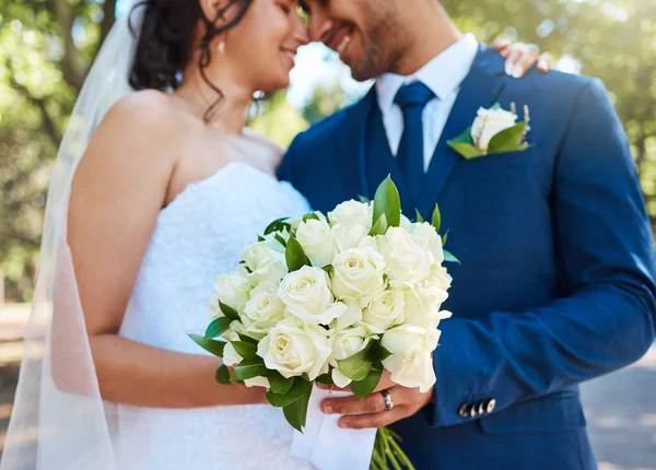 Close up of a bride in her wedding dress and groom in suit holding on to a bouquet while standing together on their wedding day. Couple tying the knot. Wedding detail.