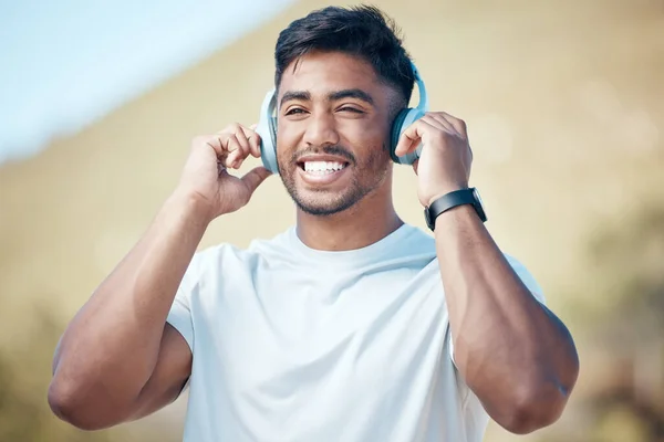 Closeup of a young indian male smiling and listening to music on wireless headphones during a exercise outside.Mixed race male smiling and listening to a song outside during a workout routine.
