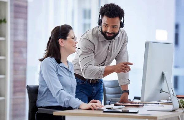 Mixed race call centre telemarketing agent training new caucasian assistant on a computer in an office. Supervisor manager troubleshooting solution with intern for customer service and sales support