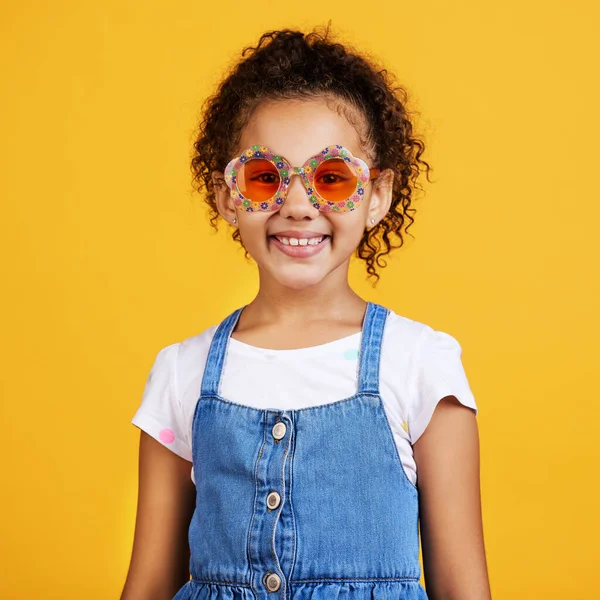 Studio portrait mixed race girl wearing funky sunglasses Isolated against a yellow background. Cute hispanic child posing inside. Happy and carefree kid with an imagination for being a fashion model.