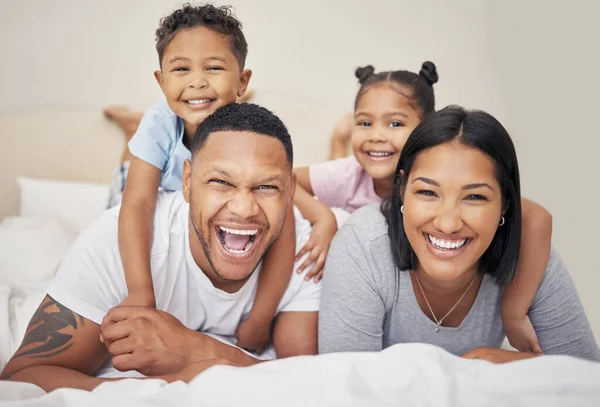 Portrait of a cheerful family lying together on bed. Little boy and girl lying on their parents laughing and having fun. Mixed race couple bonding with their son and daughter. Hispanic siblings