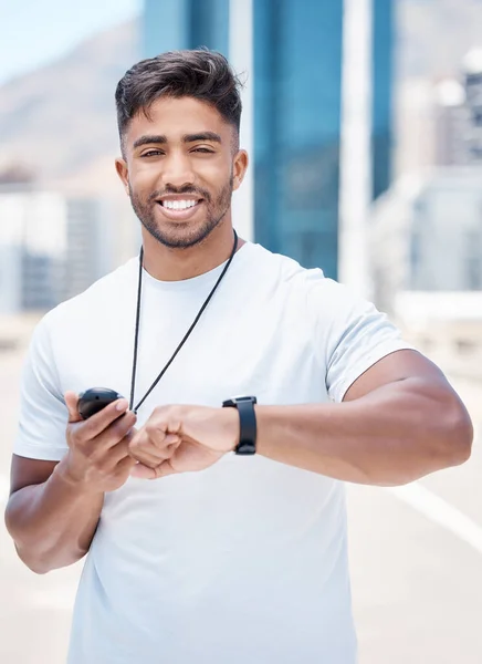 Portrait of satisfied mixed race male athlete checking digital chronometer and smart watch to track time during a workout. Sportsman monitoring his performance or progress during a run in the city.