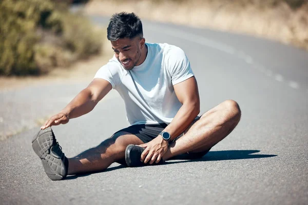 Closeup of young man sitting alone and stretching during his outdoor workout. Fit male warming up before a run outside on a road.