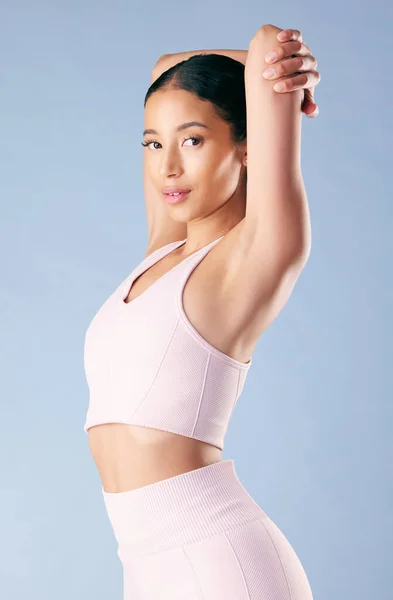 Mixed race fitness woman stretching in studio against a blue background. Beautiful young hispanic female athlete warming up for exercising or working out. Dedicated to a fit and healthy lifestyle.