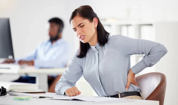 One young stressed caucasian businesswoman suffering with lower back pain in an office. Female employee feeling tense strain, discomfort and hurt to spine with poor sitting posture and long working