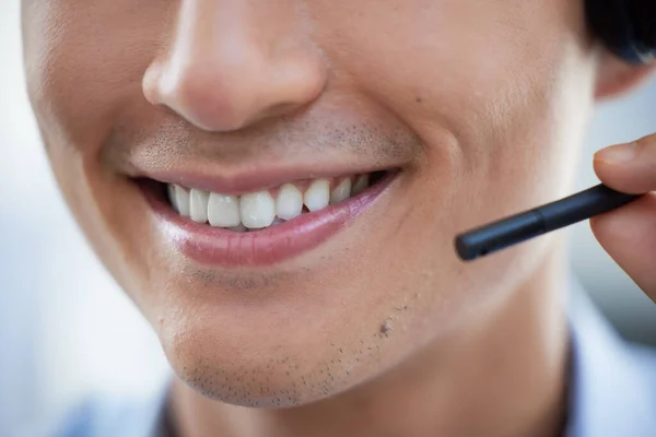 Closeup of one happy call centre telemarketing agent with big smile talking on headset while working in office. Face of confident friendly businessman operating helpdesk for customer service and sales