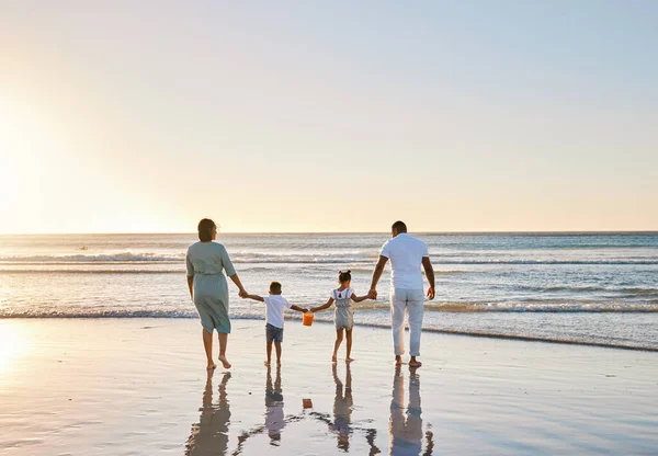 Rearview shot of a happy family walking together on the beach.