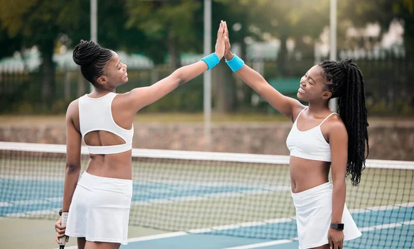 Happy friends high five on the tennis court. Two professional tennis players motivate each other after a match. African american girls bonding, celebrate and support each other.