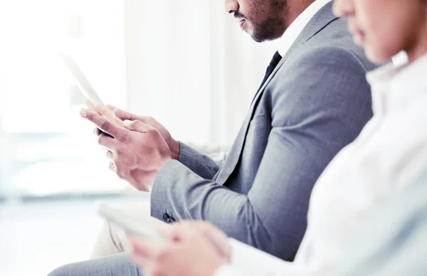 Closeup shot of an unrecognisable businessman using a digital tablet while sitting in line in an office.