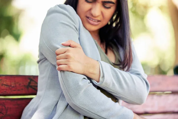 Closeup shot of a young businesswoman experiencing arm pain outdoors.