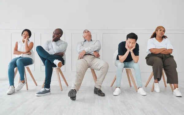 a diverse group of people looking bored while sitting in line against a white background.