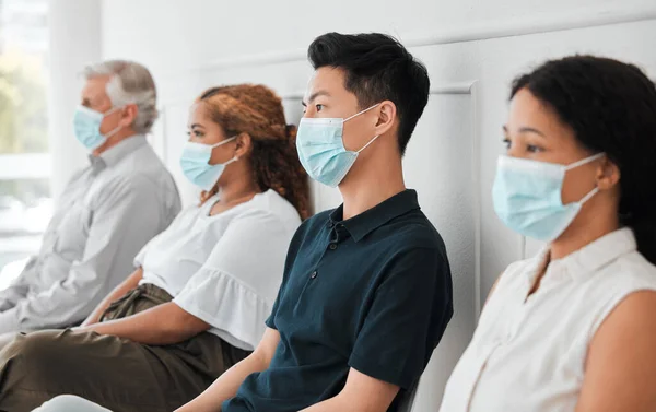 a group of people wearing face masks while sitting in a queue.