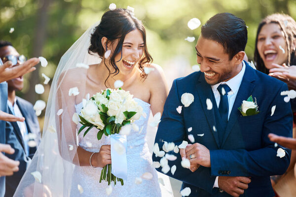 Guests throwing confetti over bride and groom as they walk past after their wedding ceremony. Joyful young couple celebrating their wedding day.