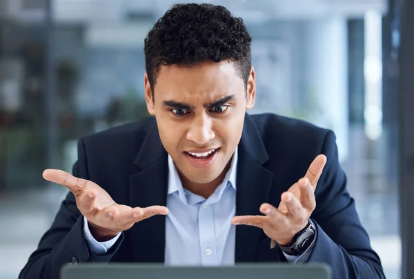 a young businessman looking annoyed while working on a laptop in an office.