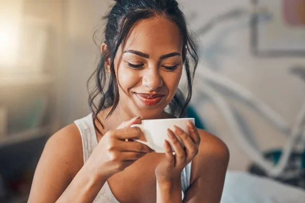 A beautiful young Hispanic woman enjoying a warm cup of coffee for breakfast. One mixed race female drinking tea while sitting in bed and daydreaming.