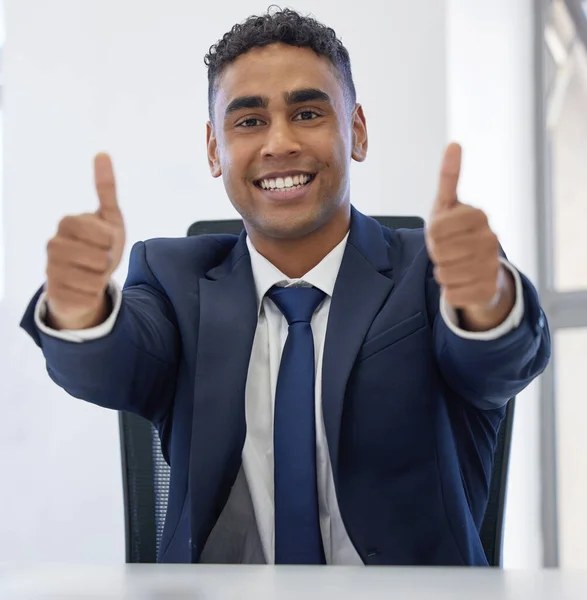 Portrait of a young businessman showing thumbs up in an office.
