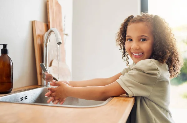 One mixed race adorable little girl washing her hands in a kitchen sink at home. A happy Hispanic child with healthy daily habits to prevent the spread of germs, bacteria and illness.