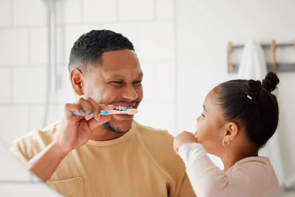 Happy mixed race father and daughter brushing their teeth together in a bathroom at home. Single African American parent teaching his daughter to protect her teeth.