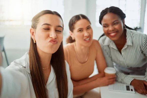Portrait of a confident young hispanic business woman making a funny face expression while taking selfies with her colleagues in an office. Group of three happy smiling women taking photos as a