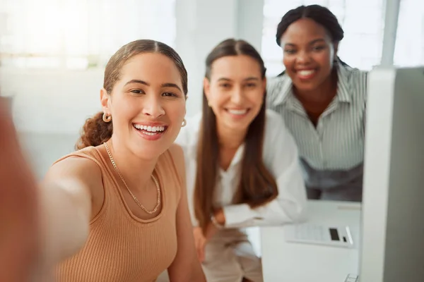 Portrait of a confident young hispanic business woman taking selfies with her colleagues in an office. Group of three happy smiling women taking photos as a dedicated and ambitious team in a creative