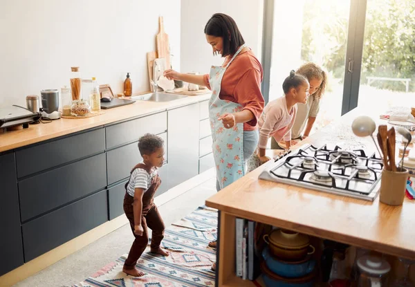 A happy mixed race family of five cooking and having fun in a kitchen together. Loving black single parent bonding with her kids while teaching them domestic skills at home.