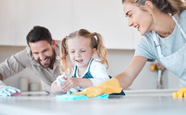 Little girl helping her parents clean. Caucasian family cleaning their kitchen together. Happy family doing housework together. Family keeping their kitchen counter clean and hygienic