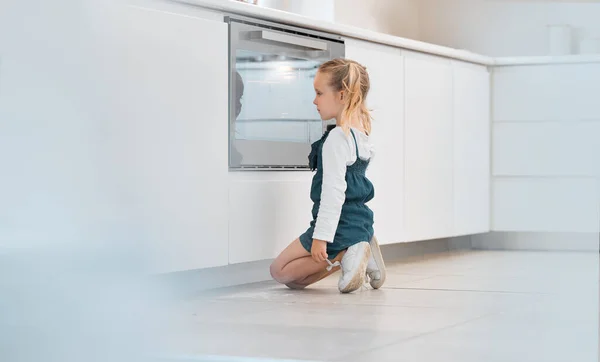 Little girl patiently waiting in front of her oven. Caucasian child waiting for her baked food. Blonde little girl looking at her food baking in the oven. Young child looking into the oven.