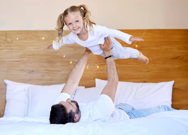 Adorable little girl bonding with her single father at home and pretending she can fly. Caucasian single parent holding and lifting his daughter in the air. Smiling child playing in the bedroom.