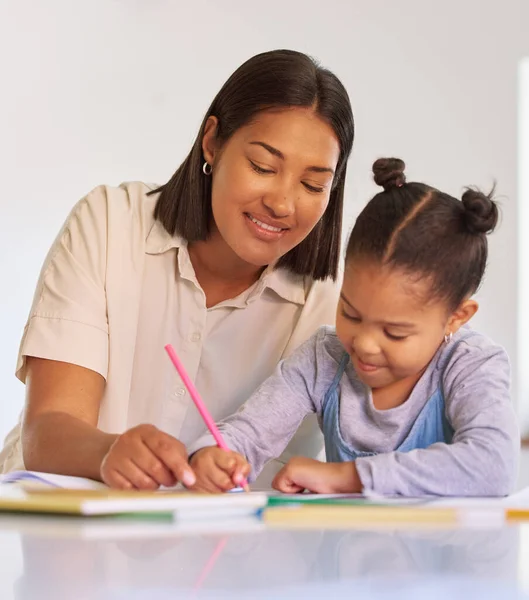 Mixed race girl learning and studying in homeschool with mom. Woman helping her daughter with homework and assignments at home. Happy parent teaching child to colour and write at home during lockdown.