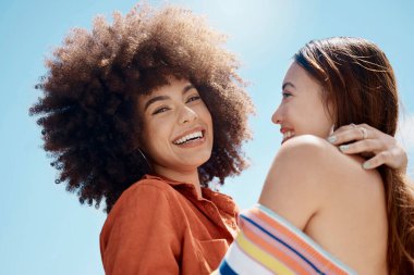 Portrait of two young mixed race female friends embrace and smiling outside on a sunny day. A Beautiful gay hispanic woman with a cool afro hair style being affectionate with her asian partner.