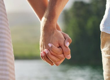 an unrecognizable couple holding hands while spending time at a lake.