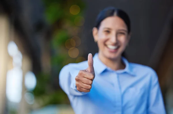 Close up of a cheerful mixed race smiling businesswoman making thumbs up gesture outside. Young hispanic woman showing a good symbol.