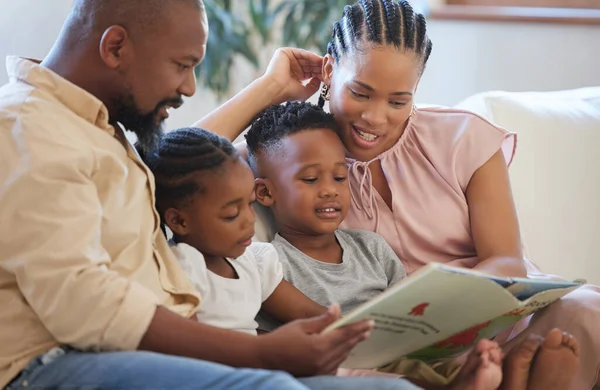 A young african american family sitting on the sofa together and smiling while reading a story book at home.